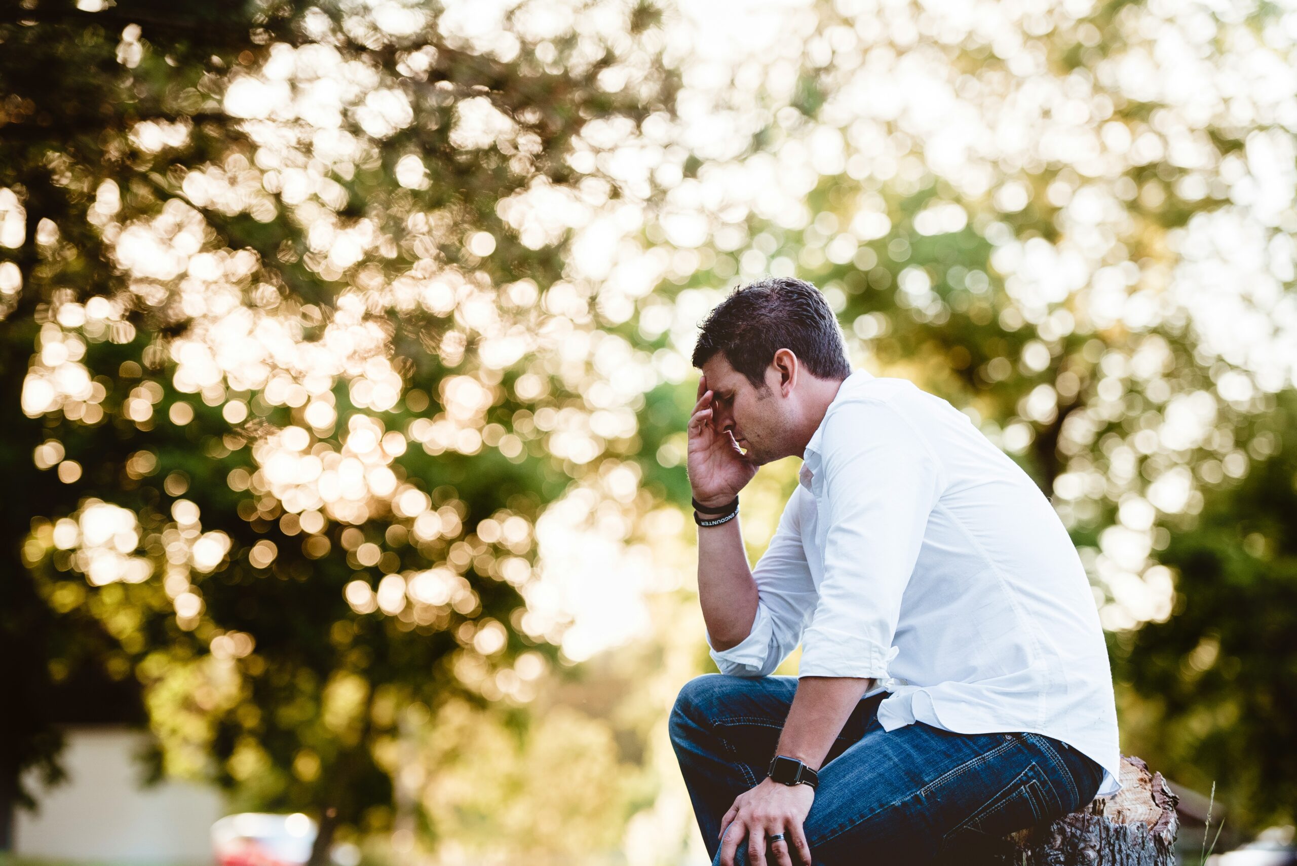 Man sitting on a bench with his hands on his face.