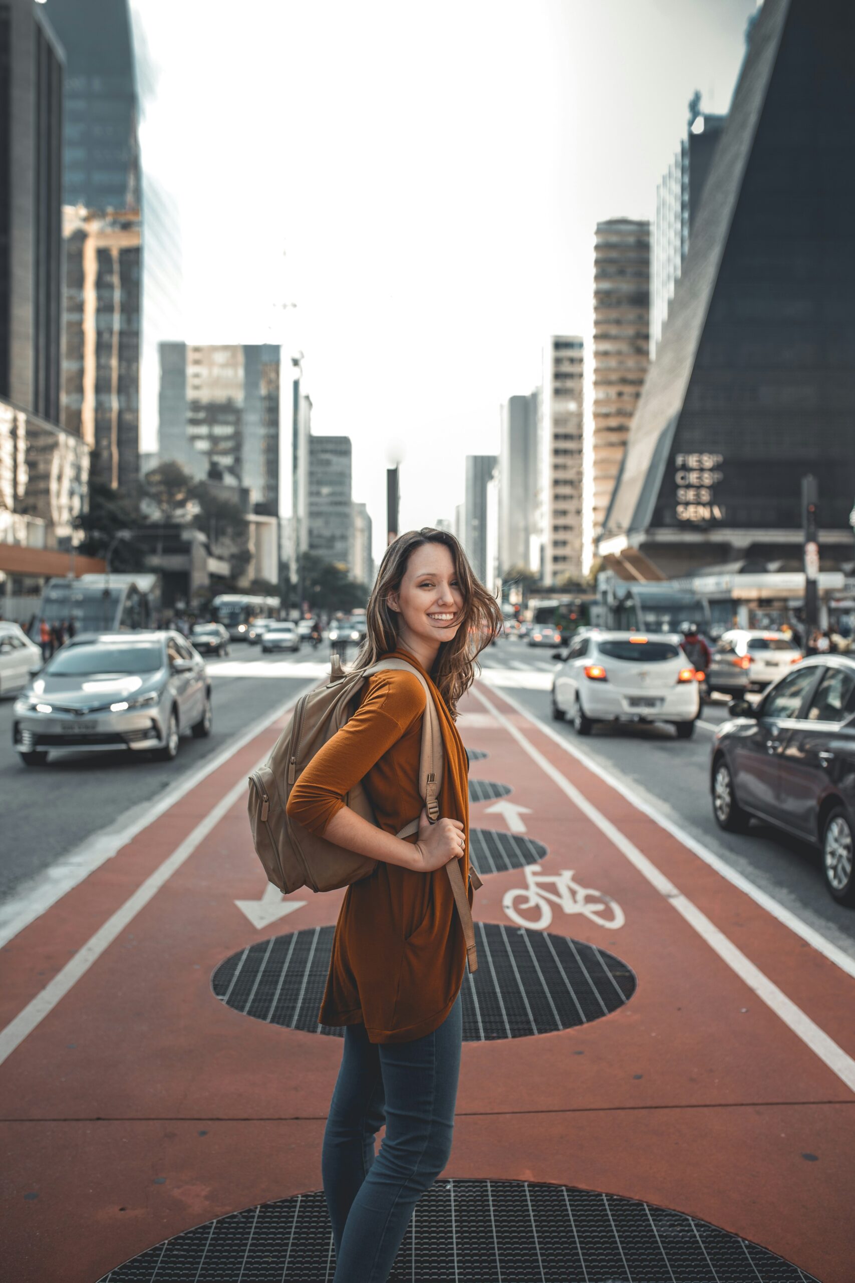 Woman with backpack on standing in the middle of a busy city street smiling