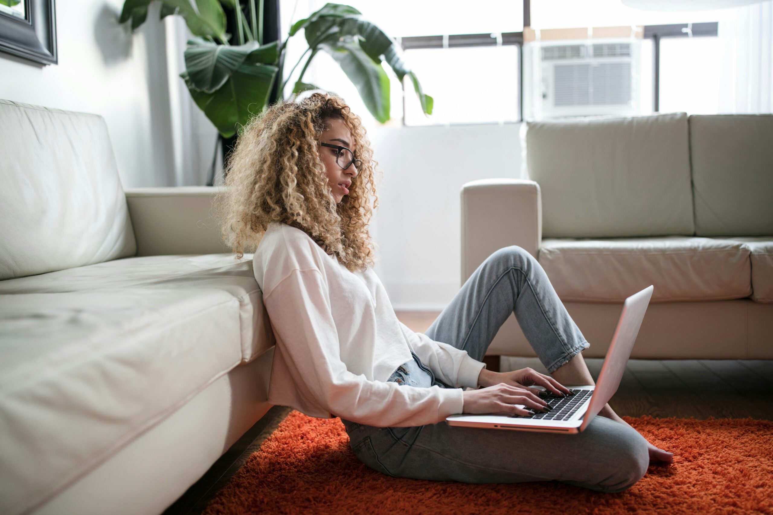 Brooklyn woman sitting on her apartment floor typing on the computer. Work life balance is possible for NY young adults.